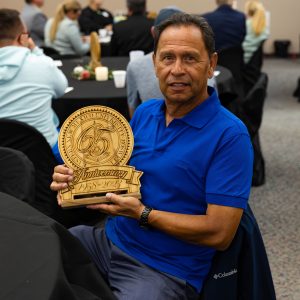 Danny Herrera, ENMU-R retiree posing with the 65th Anniversary plaque