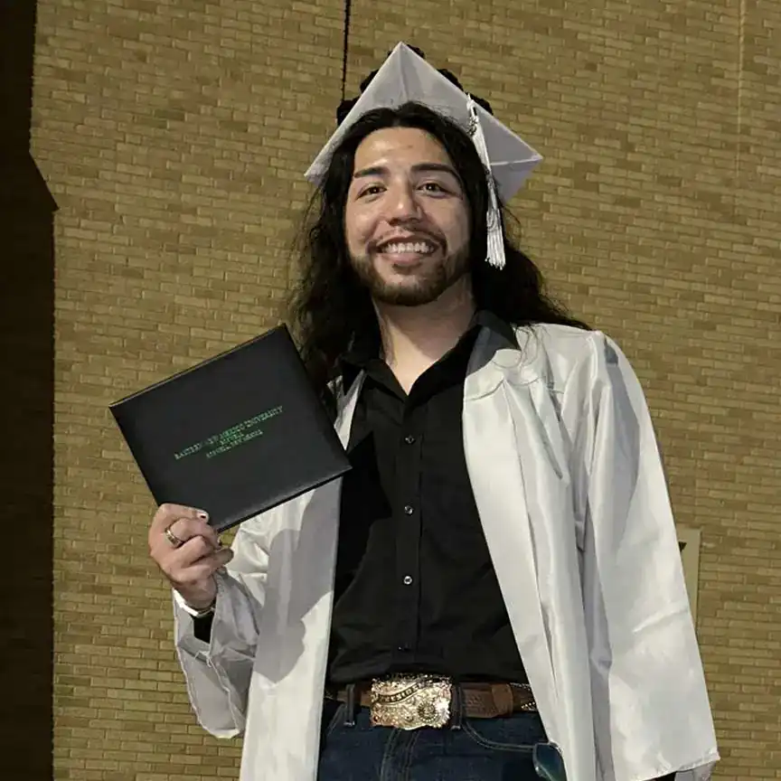 An ENMU-Roswell Student posing in a white cap and gown holding their diploma.